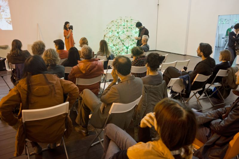 A crowd of people sitting, listening, green lights in a room